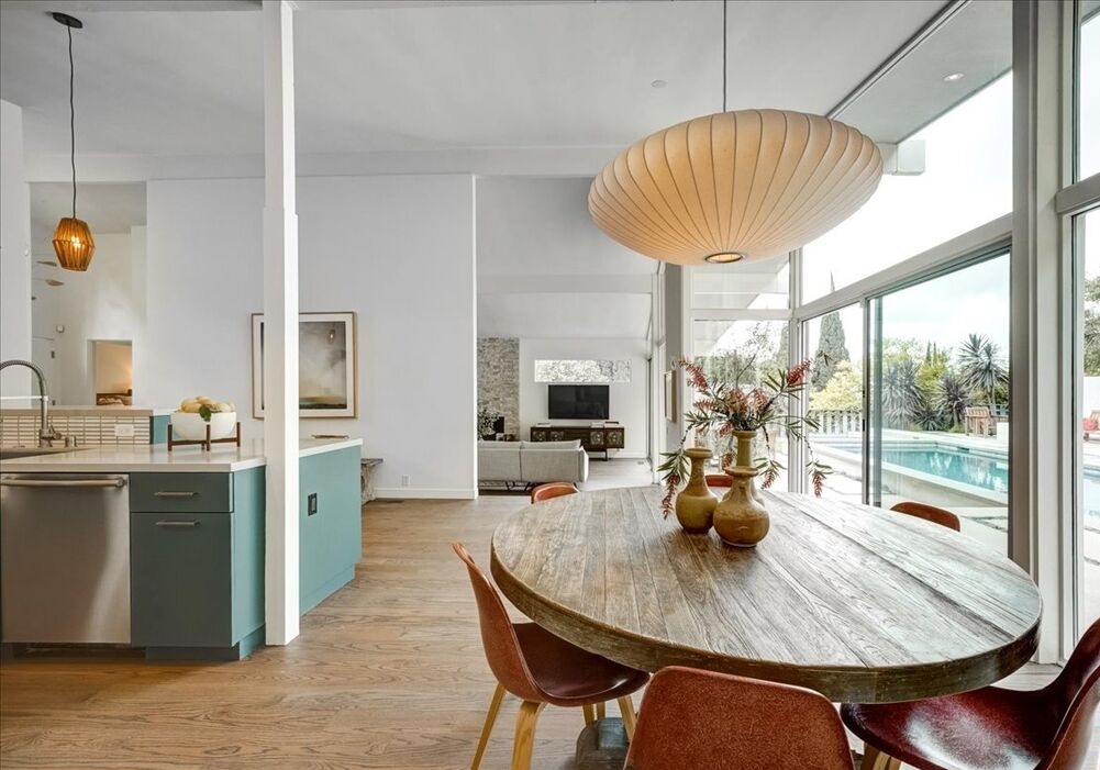 mid century architectural gem features this open dining and kitchen areas, all with walls of glass out to the rear yard and pool.