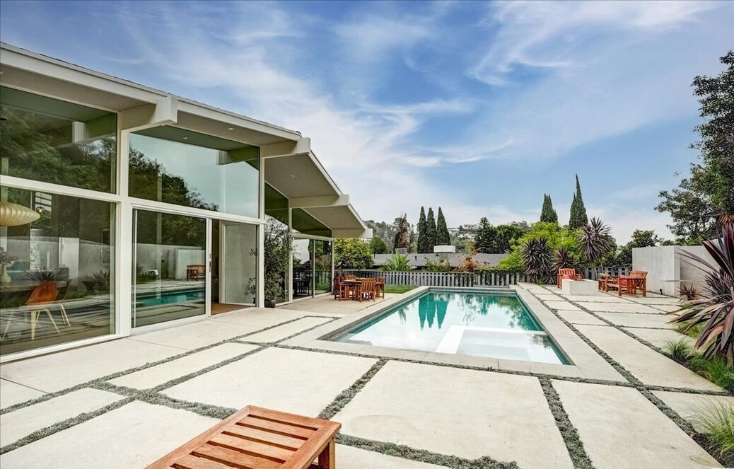 Glass walls look out to the large rear yard with lush lawn, patio area, and sparkling pool.