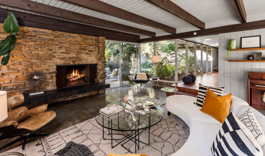 sunken living room with a cement floor, stone fireplace and walls of glass, continuing to the simple yet elegant dining room