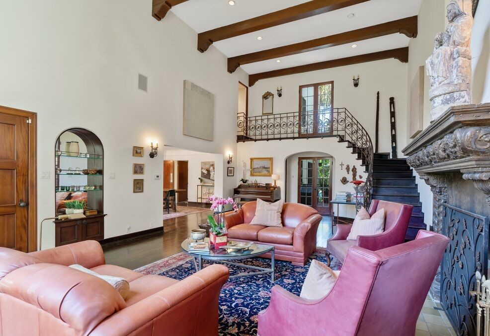 dramatic 2-Story living room with a stunning interior staircase, imposing fireplace and mantel, and a spectacular floor to ceiling leaded glass window overlooking your private front yard