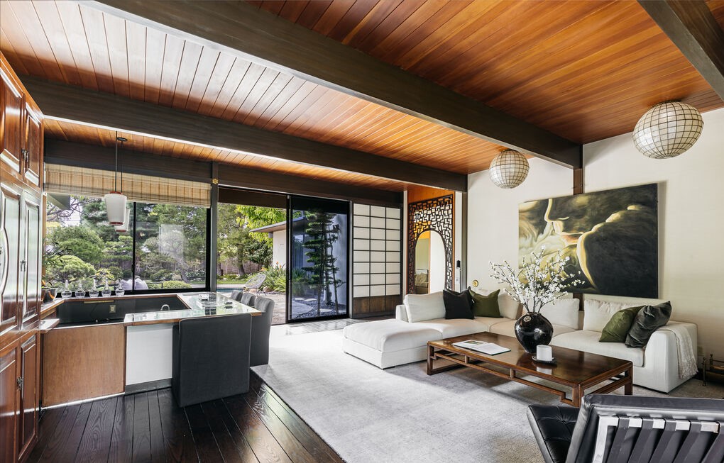 Off the entry, a formal living room with suspended mantle fireplace, exposed wood beamed ceiling, and shoji screens open to reveal calming views to the garden