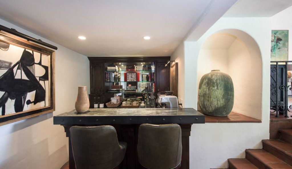 A stone driveway and steps lead to a discreet entry into a dazzling double-height living room with stenciled and beamed ceiling