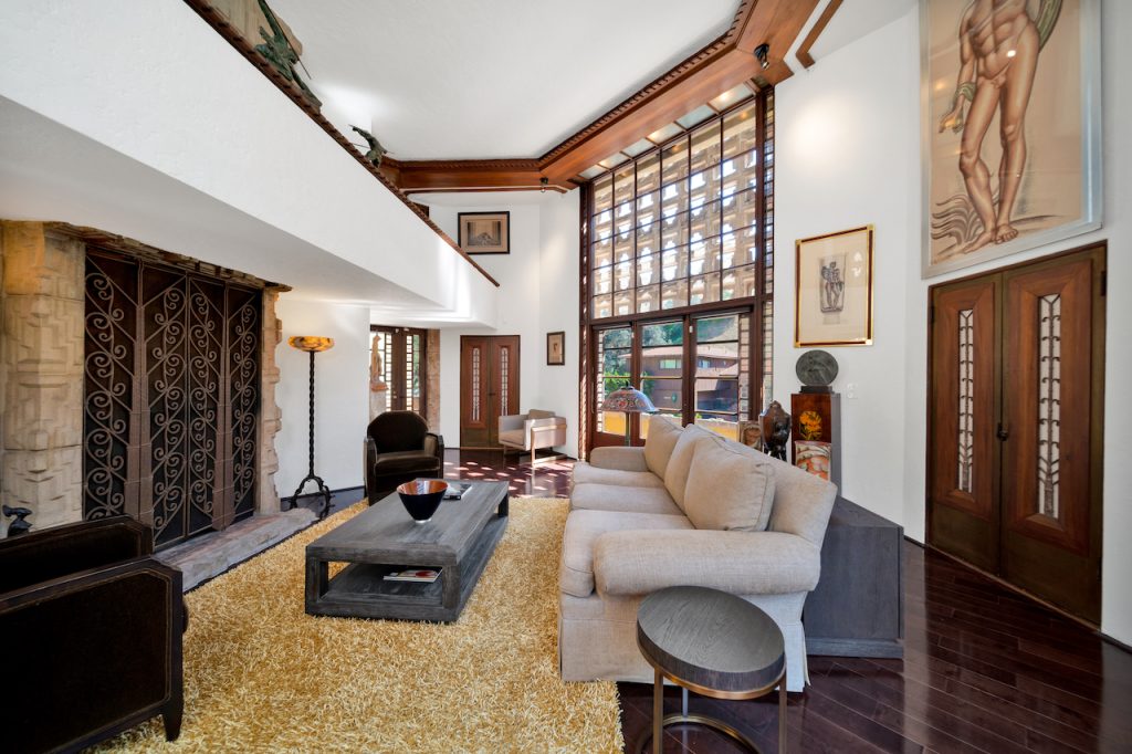 A double-storied living room features a fireplace with eight-foot-high wrought iron gates & the light dances through the blocks which overlook the mature oak trees in the garden.