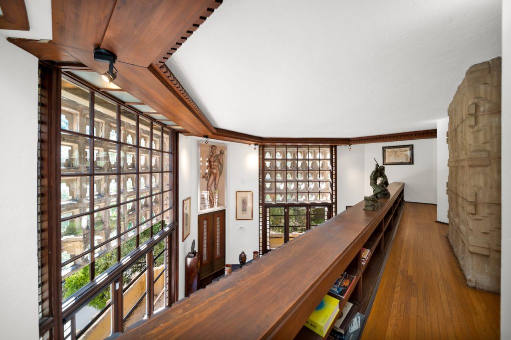 A double-storied living room features a fireplace with eight-foot-high wrought iron gates & the light dances through the blocks which overlook the mature oak trees in the garden.