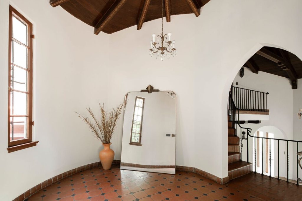 beamed ceiling in the entry rotunda, iron staircase railing, red Spanish tile and the stunning living room with open beamed ceiling and balcony.