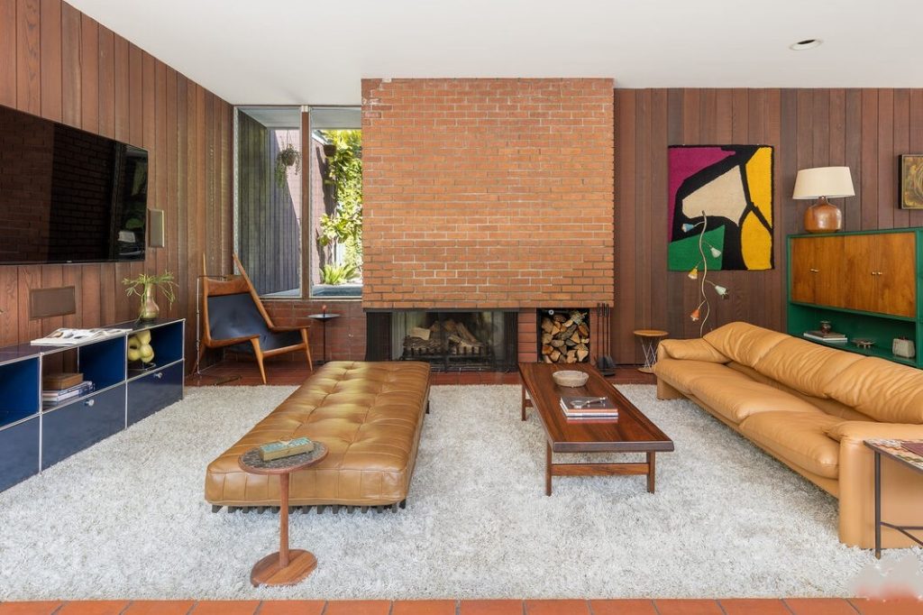 ) home showcases original features including striking floor-to-ceiling windows that offer an abundance of natural light, warm wood-paneled walls, a commanding brick fireplace, vintage tile floors, and a sunken living room